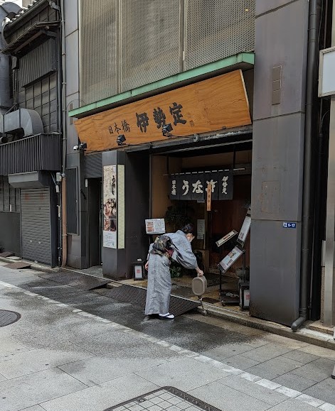 Frau reinigt den Eingang ihres Geschäfts in Nihonbashi